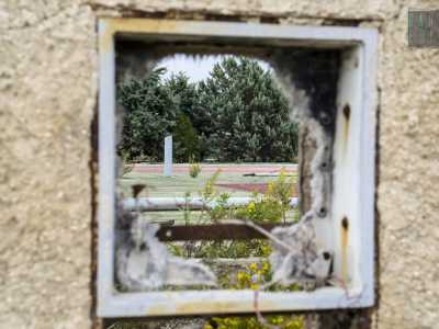 Da un buco in muro si intravedono dei campi da tennis abbandonati